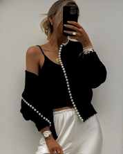 Black cardigan with pearl trim worn over black top, front view