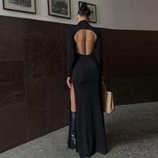 Black maxi dress with high collar and thigh-high slit, side view with handbag