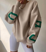 Oversized sweater beige met groene letters op mouwen, zij profiel