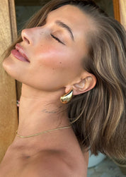 Gold teardrop earrings on model, angled side view