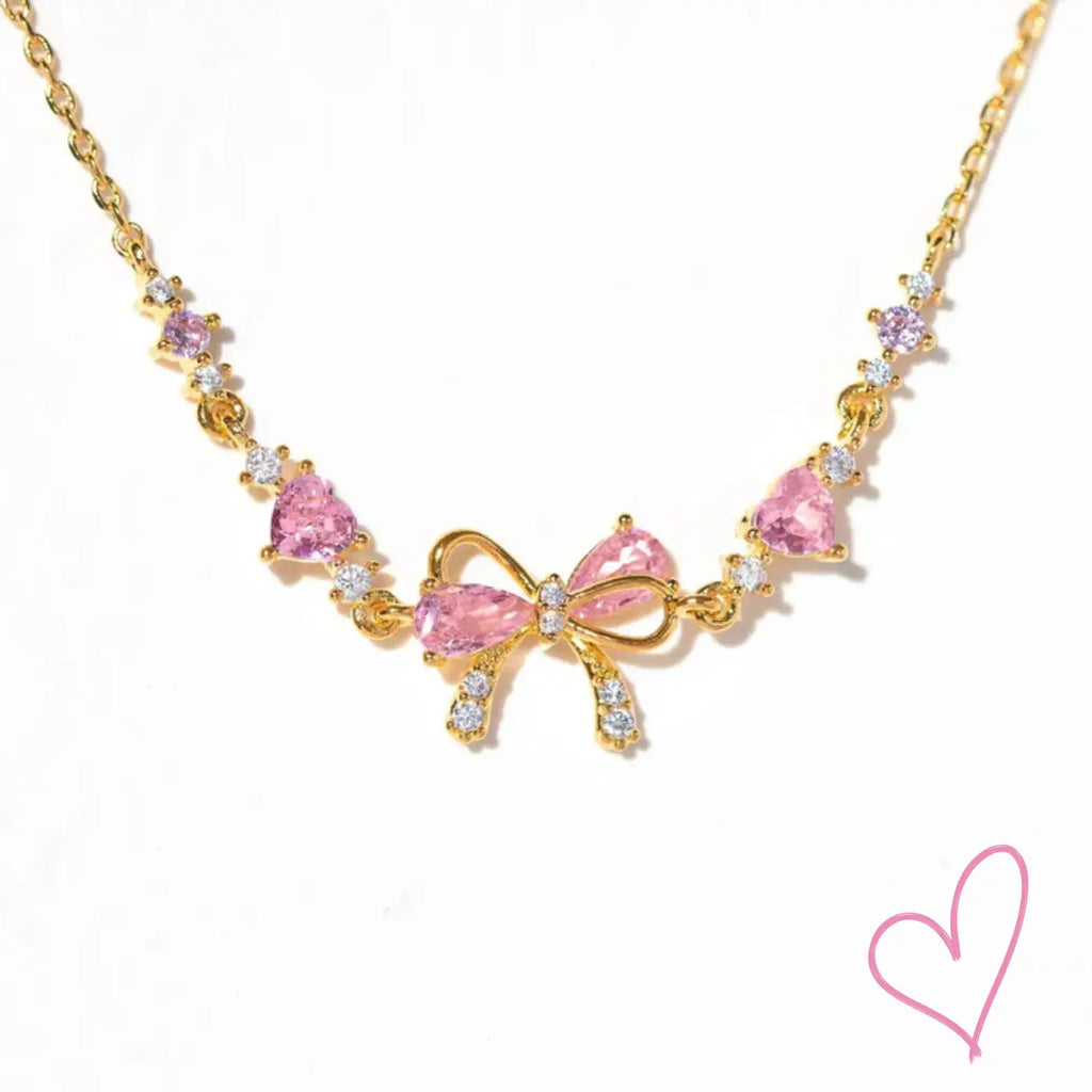 Gold necklace with pink heart stones and bow detail, front view