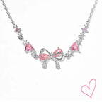 Silver necklace with pink heart stones and bow detail, front view