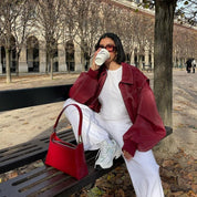 Oversized rode leren jas met witte outfit en rode tas, model zittend op bank