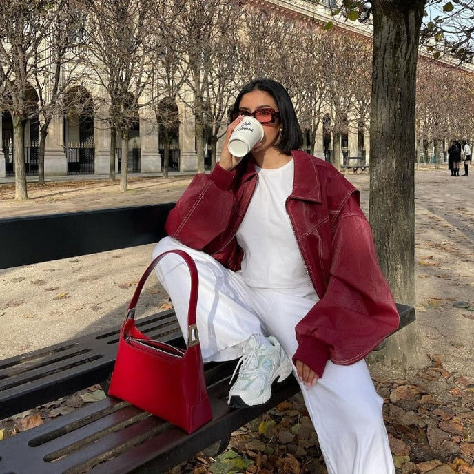 Oversized rode leren jas met witte outfit en rode tas, model zittend op bank