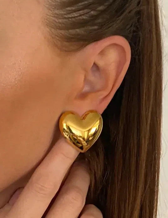 Gold heart-shaped stud earrings worn on ear close-up