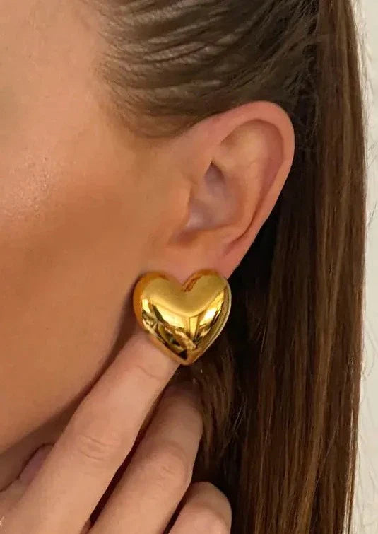 Gold heart-shaped stud earrings worn on ear close-up