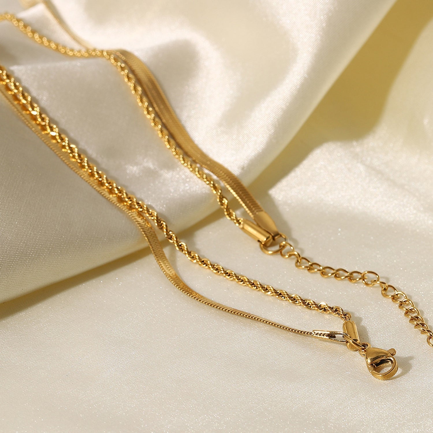 Gold-colored layered necklace with clasp on fabric background close-up