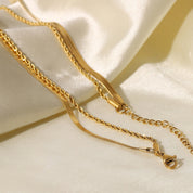 Gold-colored layered necklace with clasp on fabric background close-up