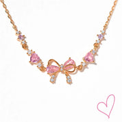 Rose gold necklace with pink heart stones and bow detail, front view