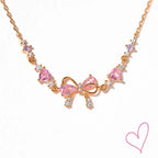 Rose gold necklace with pink heart stones and bow detail, front view