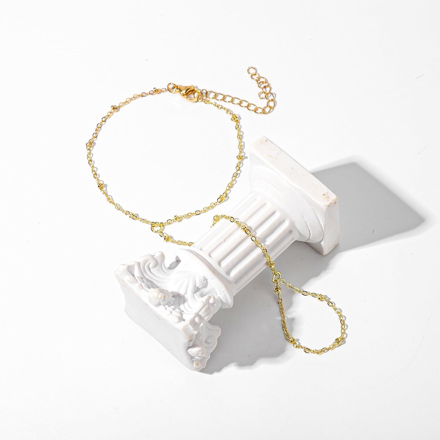 Gold chain bracelet with adjustable design displayed on white column