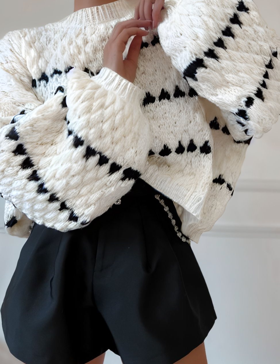 Close-up of cream chunky knit sweater with black heart pattern, highlighting texture and detail