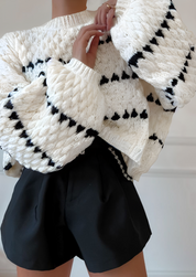 Close-up of cream chunky knit sweater with black heart pattern, highlighting texture and detail