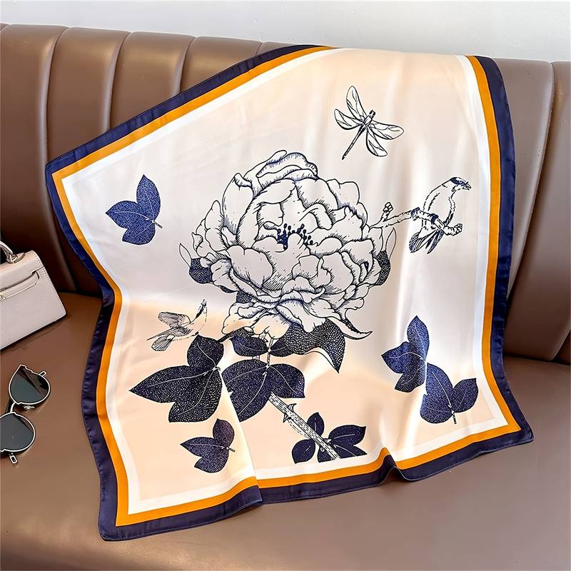 Silk scarf with floral and bird print, blue and orange border, laid flat on leather surface