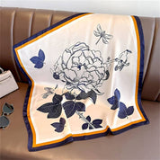 Silk scarf with floral and bird print, blue and orange border, laid flat on leather surface