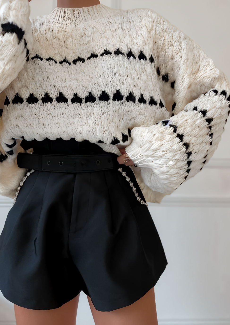 Cream chunky knit sweater with black heart pattern, worn with black shorts, front view with hand on hip