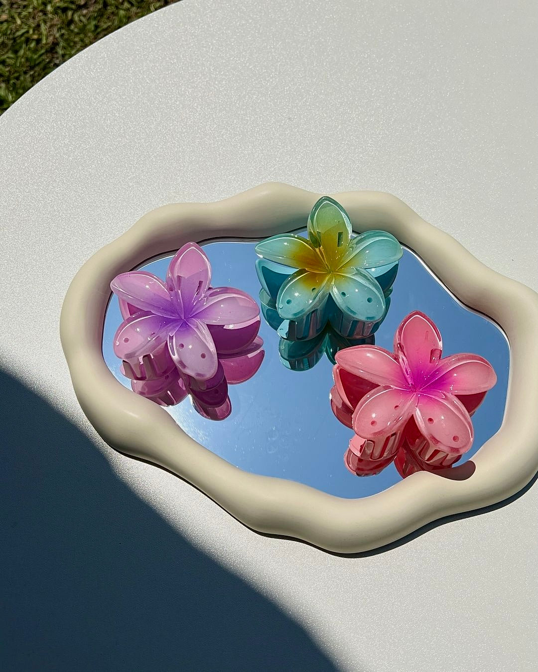 Flower-shaped hair clip with gradient colors purple, pink, and blue on a heart-shaped tray.