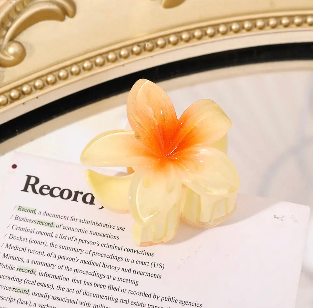 Yellow flower-shaped hair clip with gradient petals on a book page.
