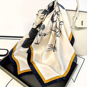 Silk scarf with floral and bird print, blue and orange border, draped over a handbag