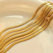 Stacked gold herringbone necklaces on white surface