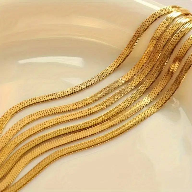 Stacked gold herringbone necklaces on white surface