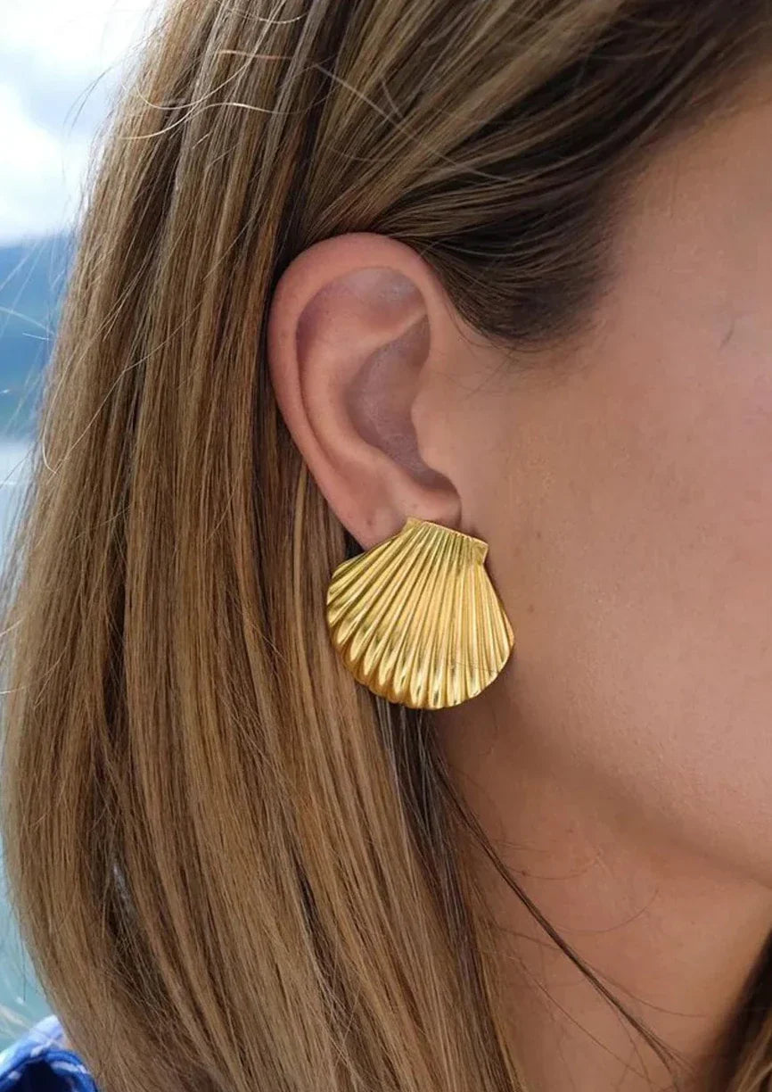 Gold shell-shaped earrings on ear side view