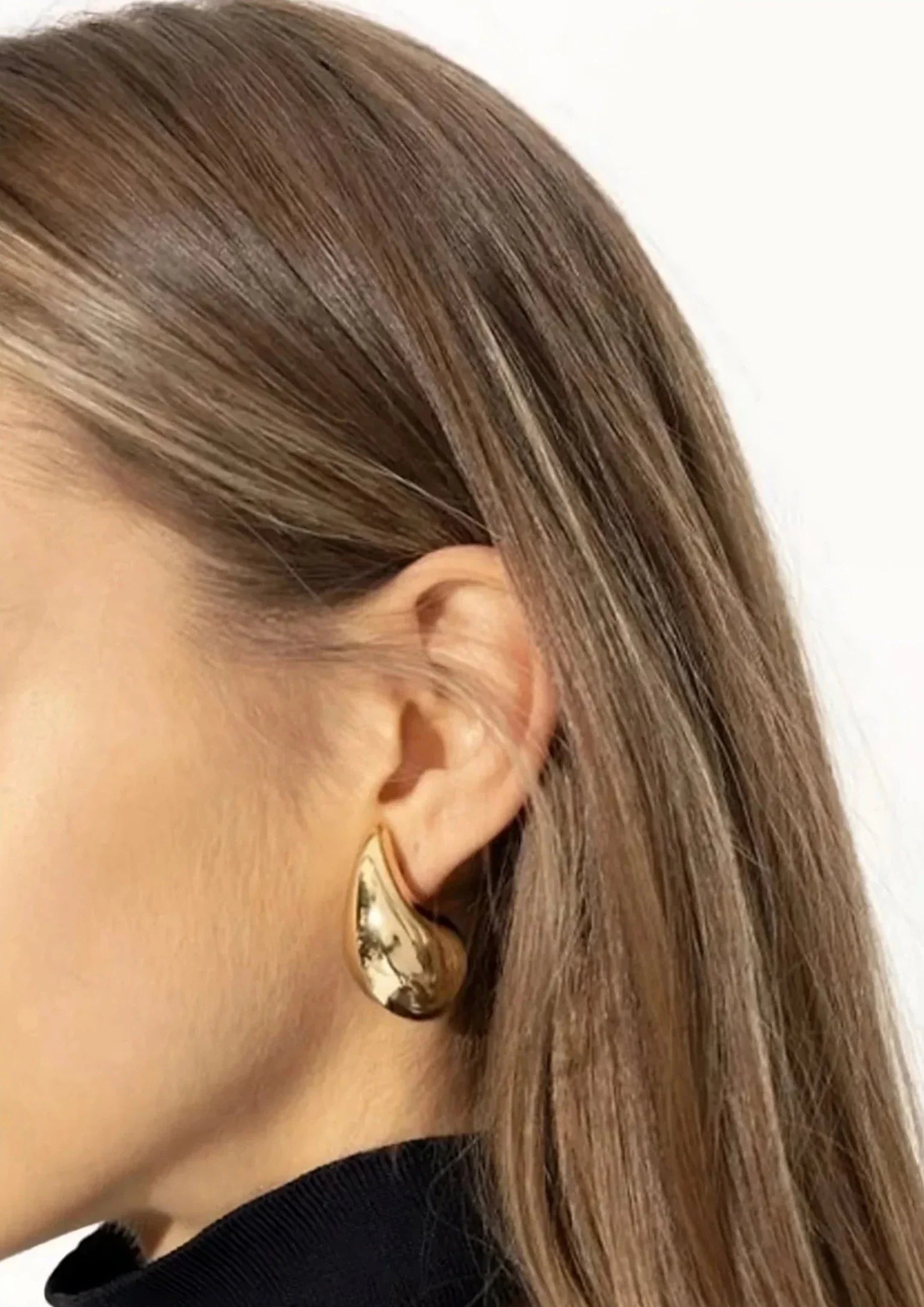 Gold teardrop earrings on model, close-up ear view