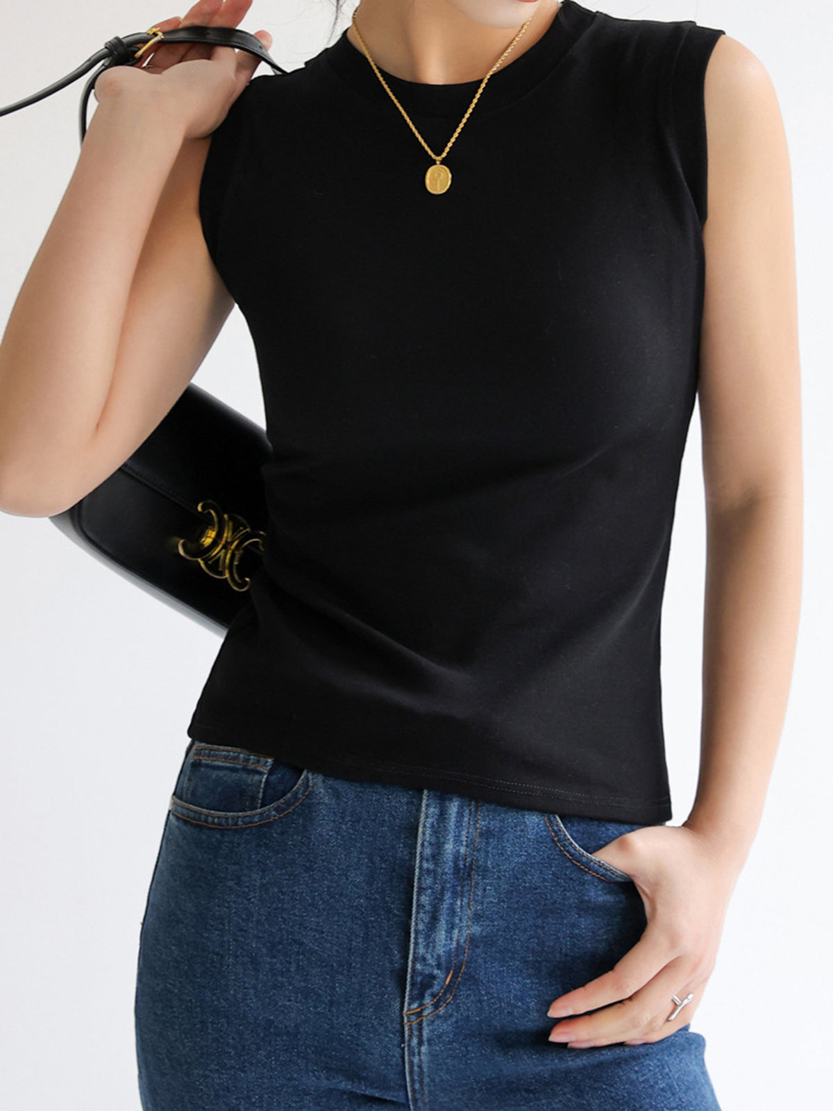 Black sleeveless mock-neck top worn with jeans and black bag front view