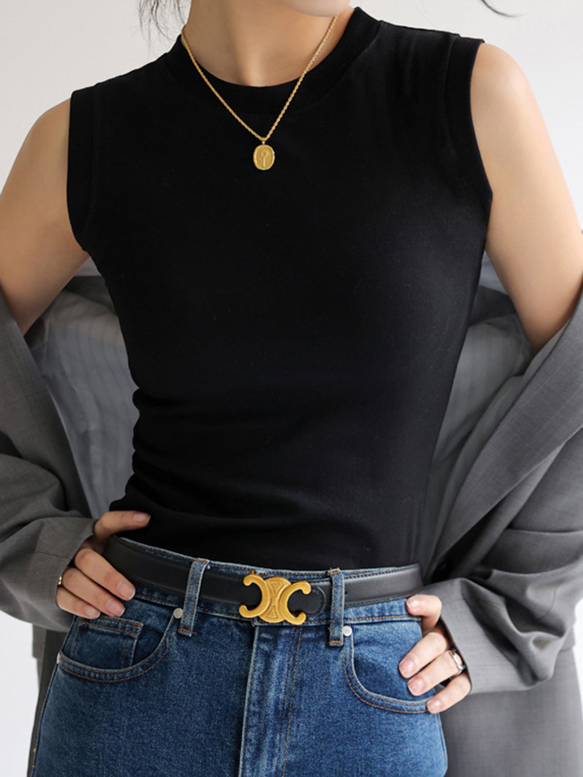 Black sleeveless mock-neck top worn with gray blazer and jeans front view