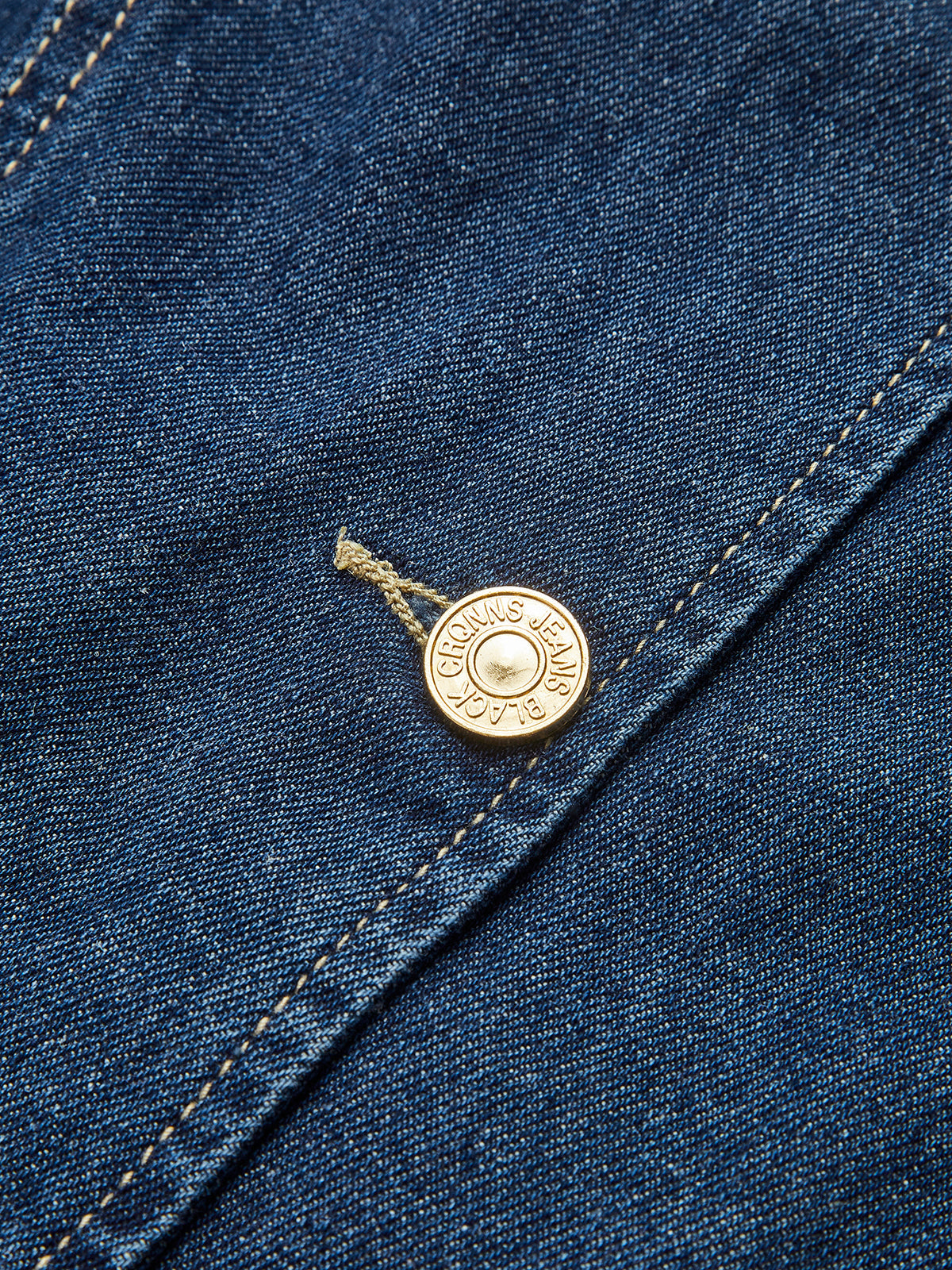 Close-up of gold button on denim fabric with stitching detail