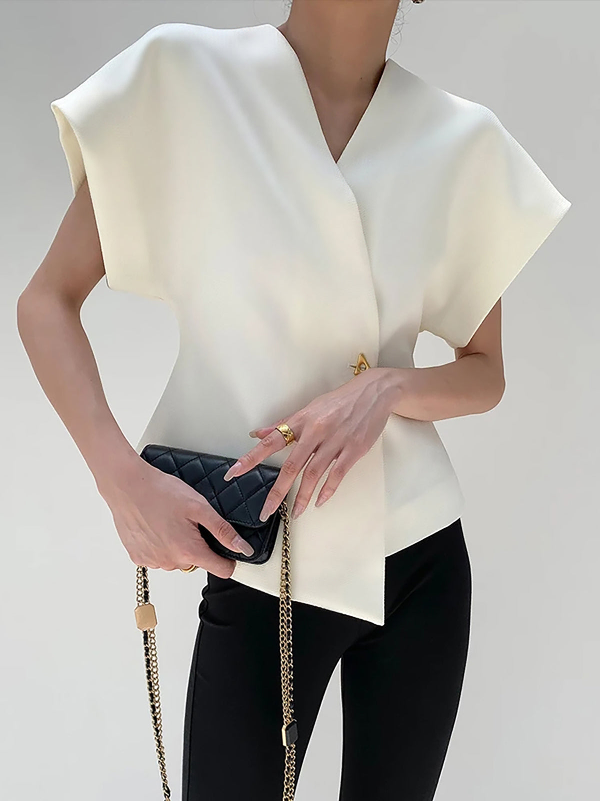 White V-neck top with gold button detail, front view with handbag