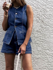 Woman wearing denim playsuit with gold buttons and pockets, holding coffee cup