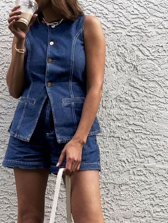 Woman wearing denim playsuit with gold buttons and pockets, holding coffee cup