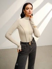 Khaki high-neck top with gold accessories and black jeans pose