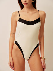 Woman wearing white swimsuit with black contrast straps, standing pose