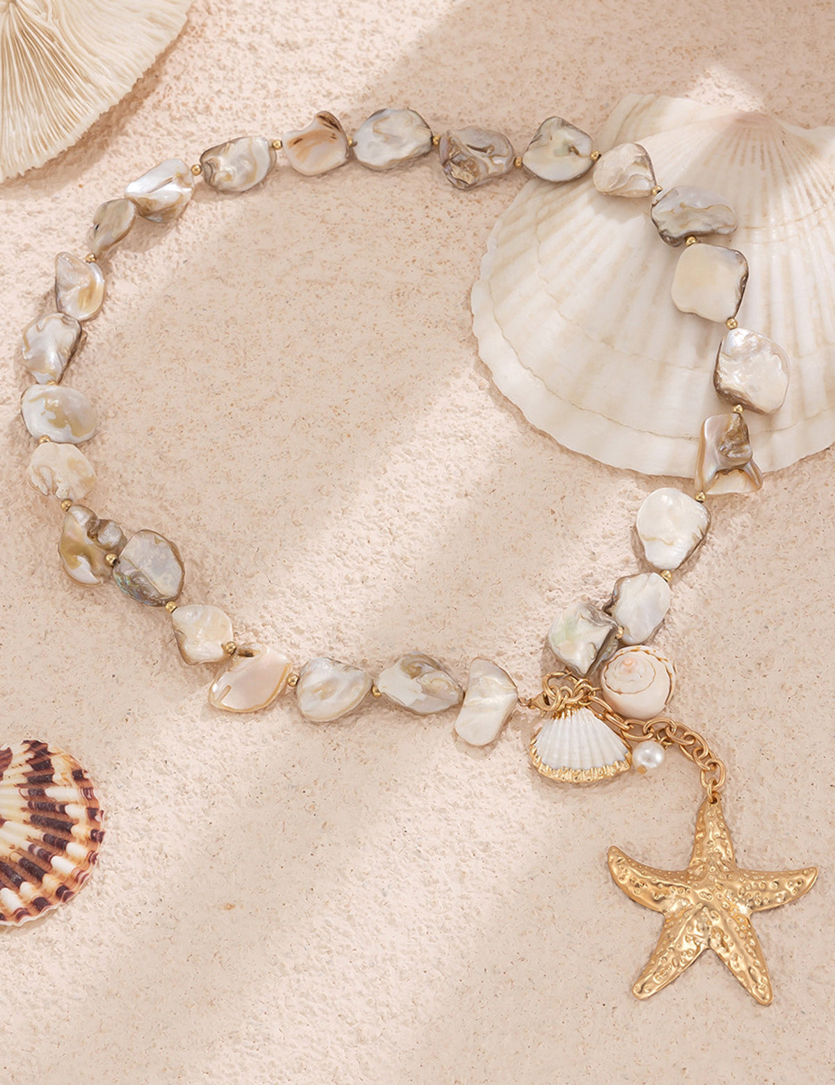 Necklace with gold starfish pendant and shell beads, overhead view on sandy background