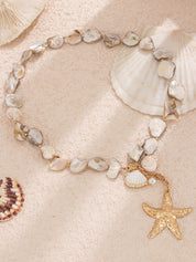 Necklace with gold starfish pendant and shell beads, overhead view on sandy background