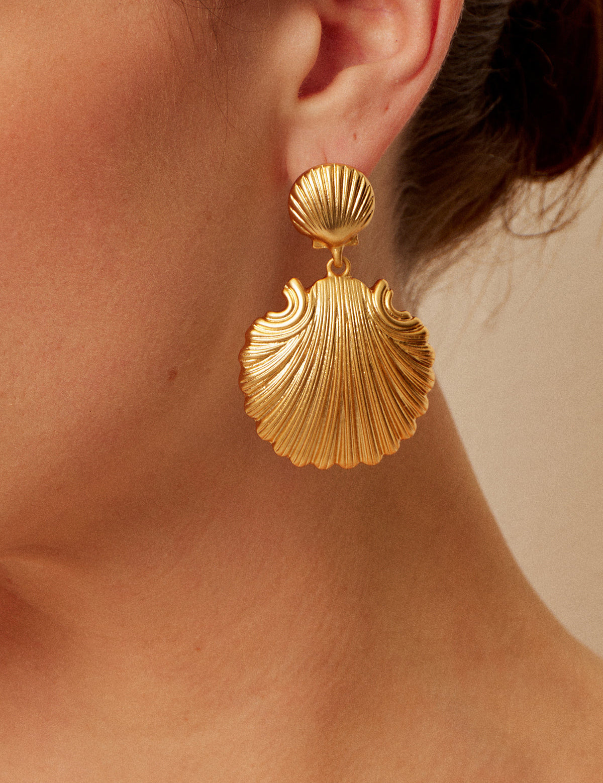 Gold shell-shaped earrings with textured detail, close-up side view
