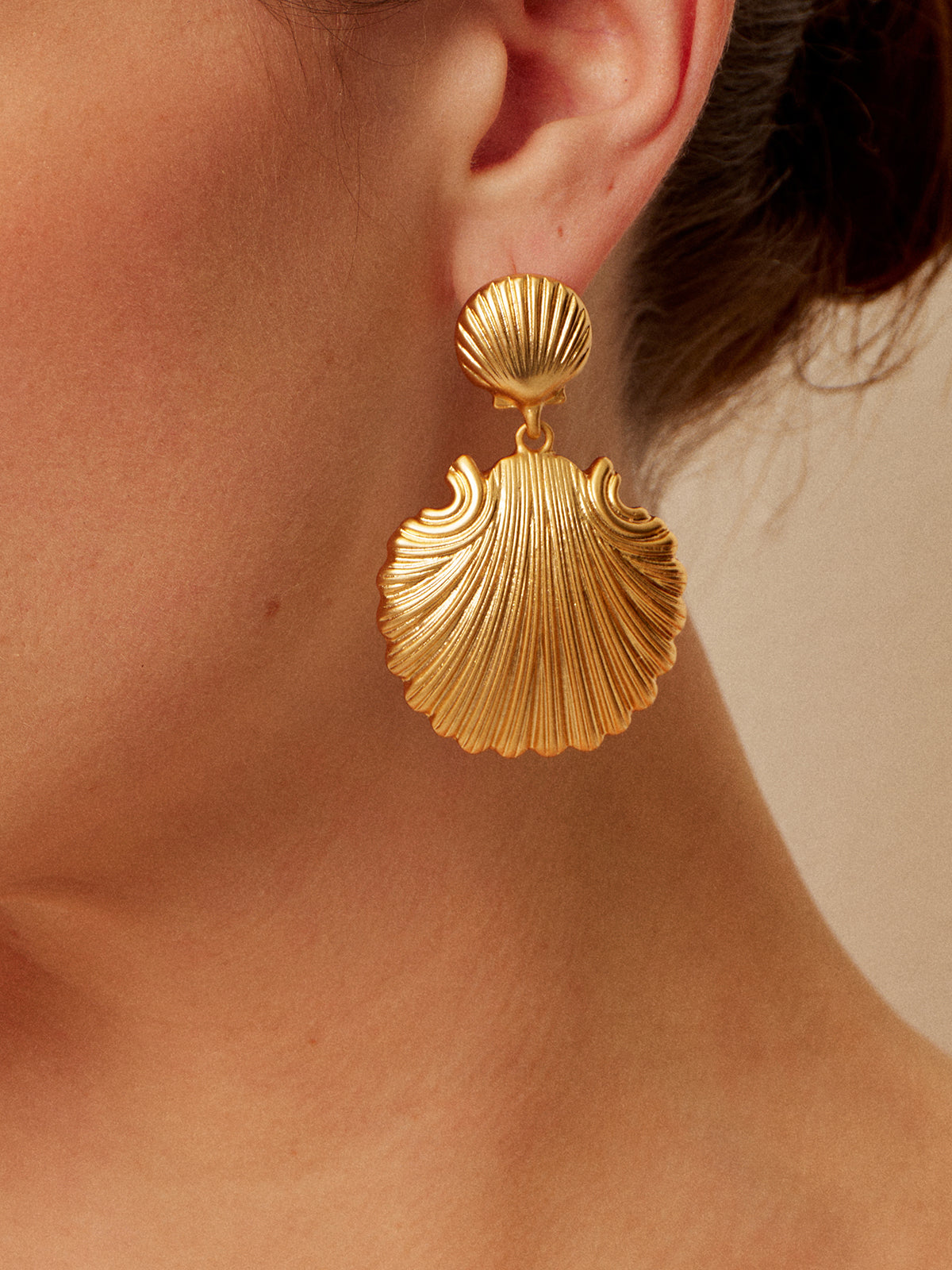 Gold shell-shaped earrings with textured detail, close-up side view