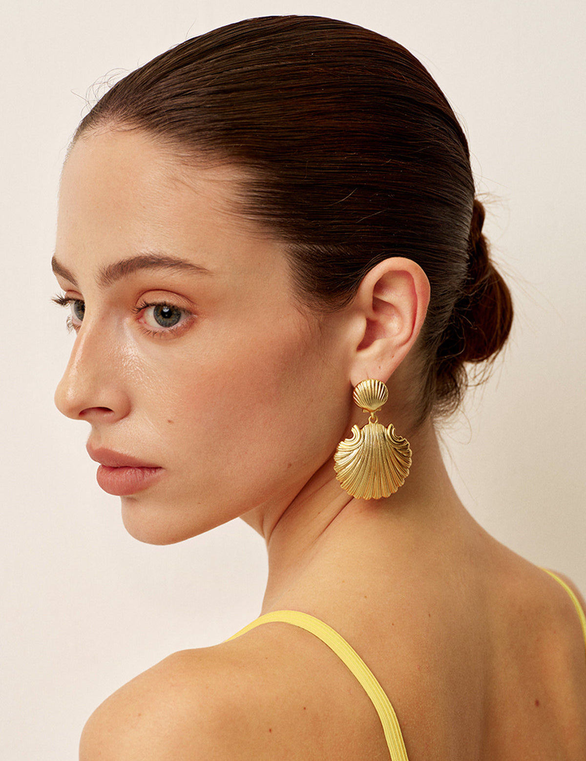 Gold shell-shaped earrings with textured detail, worn on ear, side view