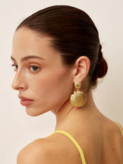 Gold shell-shaped earrings with textured detail, worn on ear, side view