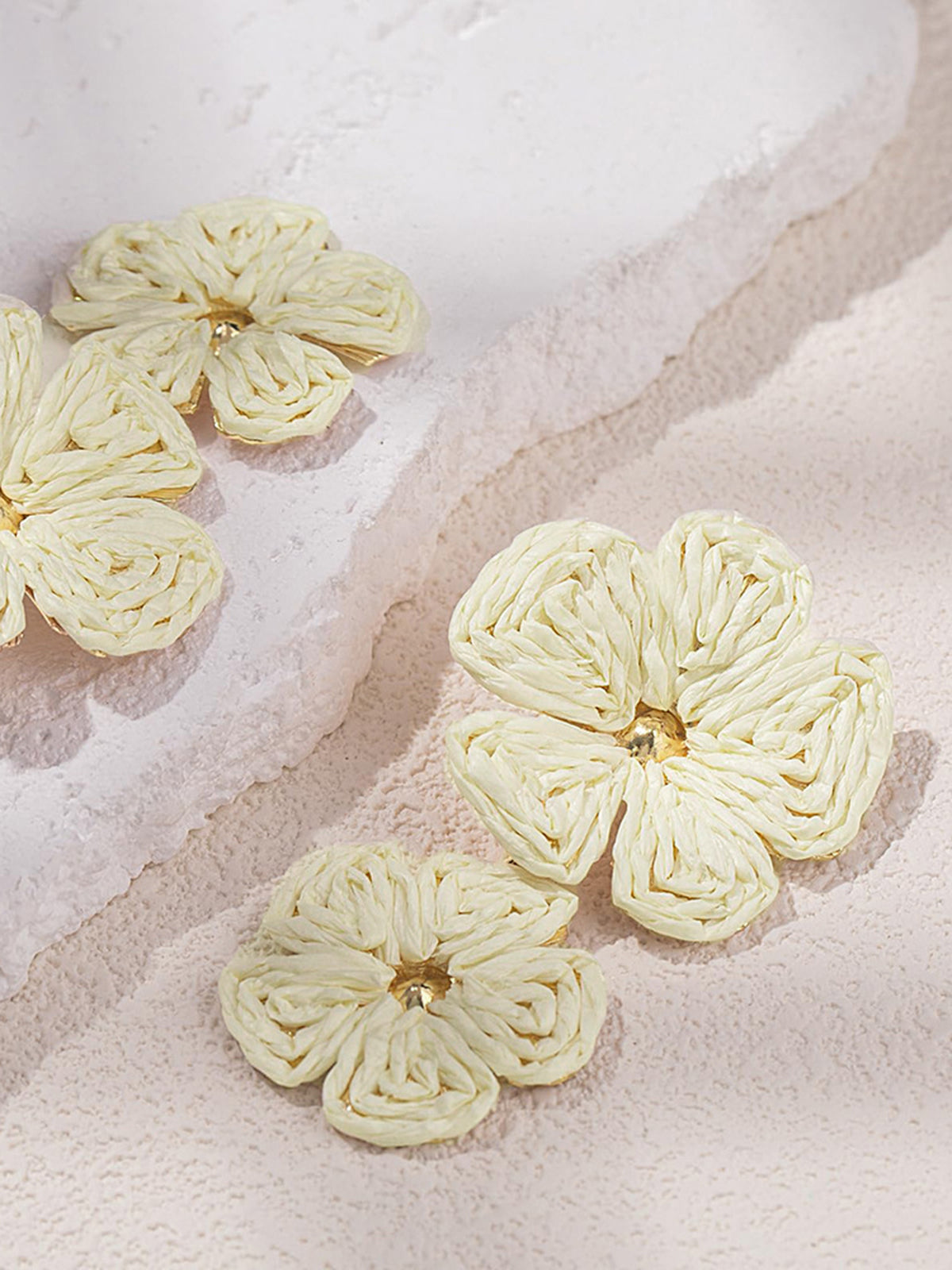White woven raffia flower earrings on textured surface