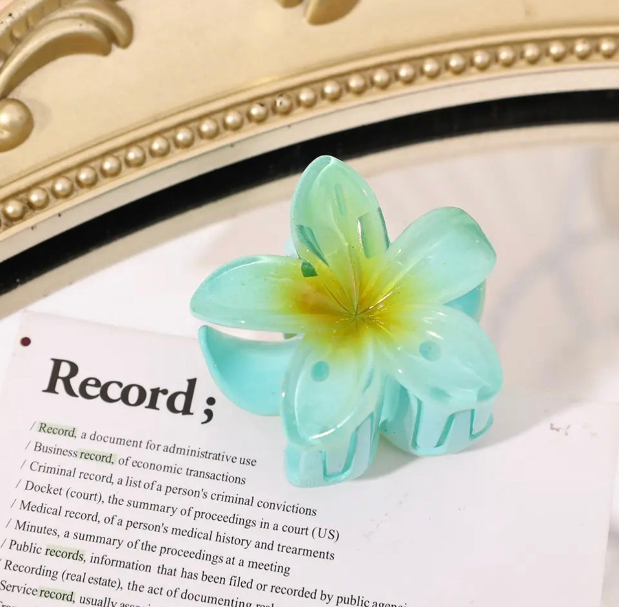 Green flower-shaped hair clip with gradient petals on a book page.
