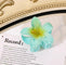 Green flower-shaped hair clip with gradient petals on a book page.