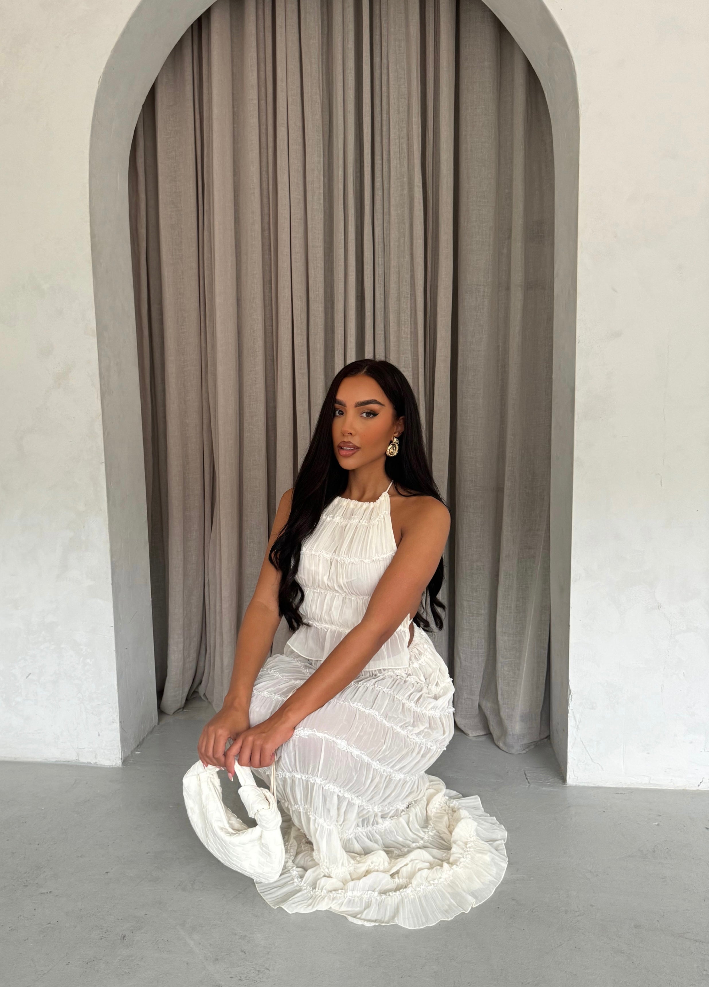 White pleated maxi dress with halter neck, seated front view