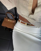 Brown leather belt with gold buckle worn with white skirt