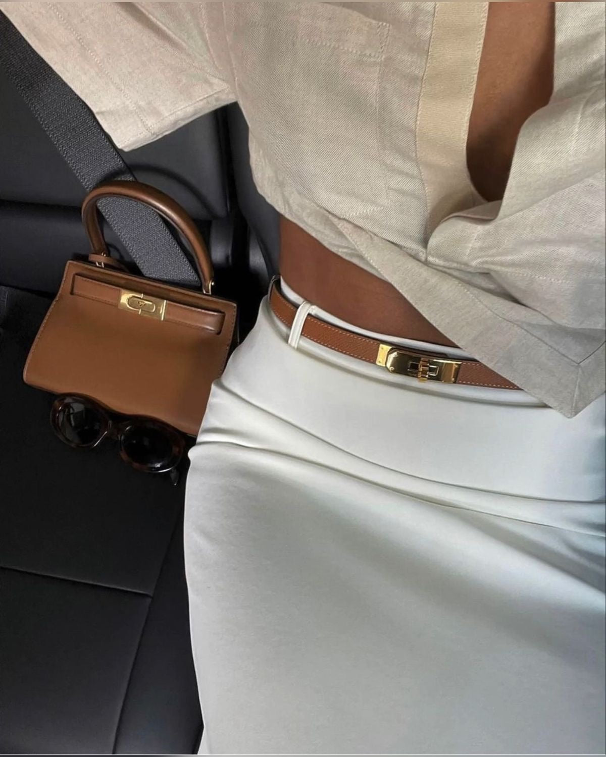 Brown leather belt with gold buckle worn with white skirt