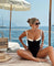 Elegante zwempak zwart met witte details, vrouw zittend op strand, front view