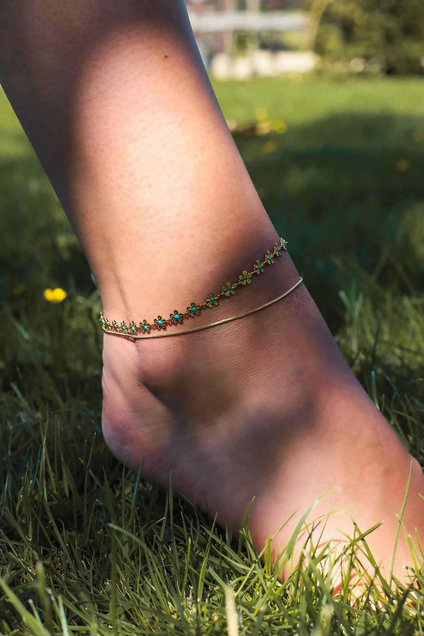 Gold anklet with floral beads on foot, grass background
