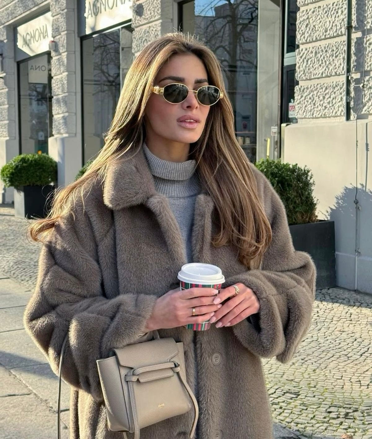 Woman wearing gold-rimmed sunglasses with beige coat and purse